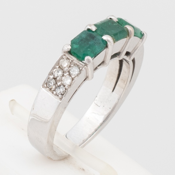 Anel em ouro branco 18 K com três esmeraldas de aproximadamente 35 pontos cada e doze brilhantes de aproximadamente 2 pontos cada. Aro 15,5. Peso 6,7 gr. (Por medida de segurança esse lote não se enco