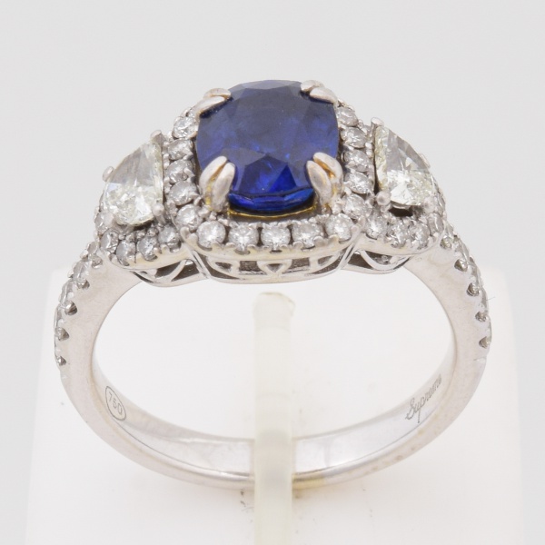 Anel em ouro branco, contrastado 750 k, com safira azul central de aproximadamente 1,20 cts cravejado de brilhantes, sendo dois lapidação meia lua nas laterais e quarenta e sete redondos. Aro 16. Peso