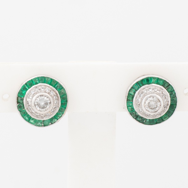 Par de brincos em ouro branco, 18 k com dois diamantes centrais de aproximadamente 25 pontoa cada, rodeados de esmeraldas, cravejado com diamantes. Med. 1,3 cm diâm. Peso 5,3 gr. (Por medida de segura