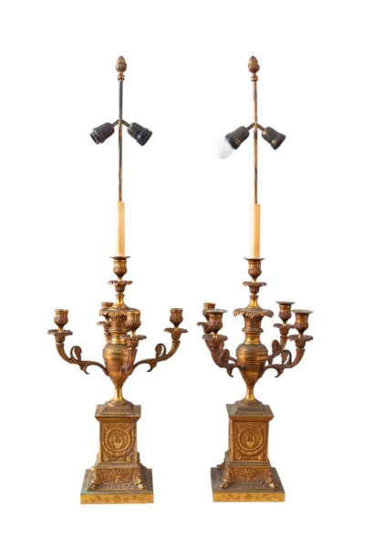 Par de candelabros eletrificados em metal dourado estilo clássico, com cinco braços para velas cada, hastes superiores com soquetes para iluminação e bases quadradas ricamente ornamentadas em relevo.