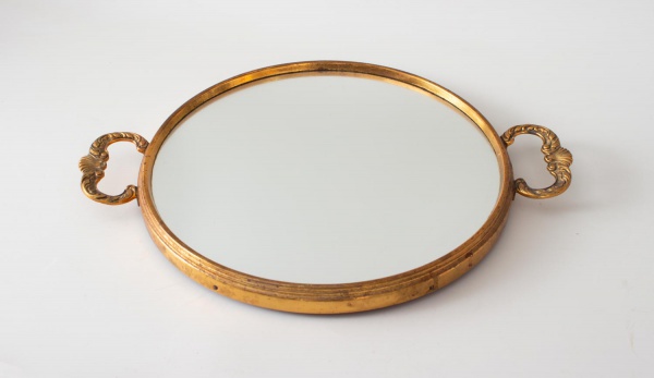Bandeja espelho circular com moldura e alças em metal dourado, estilo Luís XV. Superfície em espelho bisotado emoldurado por aro dourado com frisos, encimado por duas alças simétricas em metal fundido