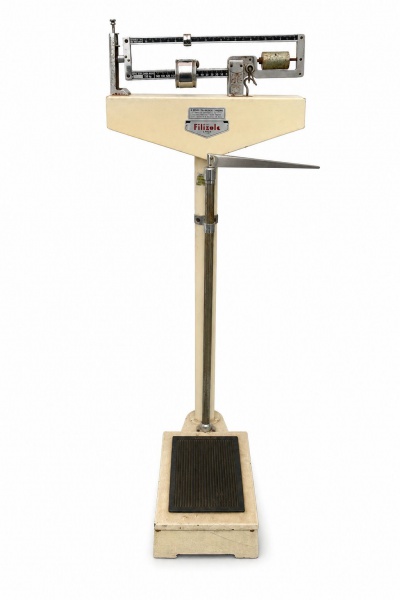 Balança mecânica Filizola com plataforma antiderrapante e coluna metálica; capacidade para 150 kg, com marcas do tempo e oxidação. Altura 134 cm.