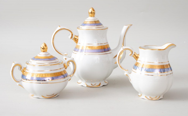 Conjunto em porcelana marca Rio Branco Guanabara composto por 1 bule, 1 leiteira e 1 açucareiro; decoração em branco, dourado e azul; altura do maior 18 cm; apresenta sinais de uso, desgastes e marcas