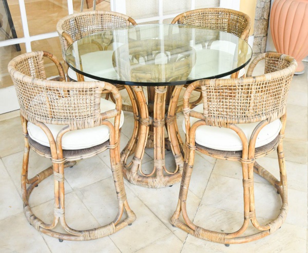 Conjunto de varanda em rattan e vime, estilo tropical/colonial, séc. XX, composto por mesa redonda com tampo em vidro fumê sobre base em bambu curvado entrelaçado e quatro cadeirões com encosto cilínd