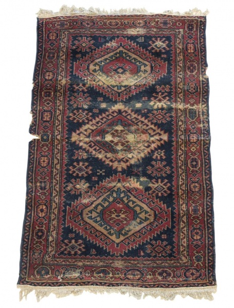 Tapete oriental artesanal, medindo 153 x 96 cm, com decoração geométrica policromada em tons de azul, vermelho e bege; apresenta desgastes acentuados, perdas nas bordas, falhas, desfiados, manchas e s