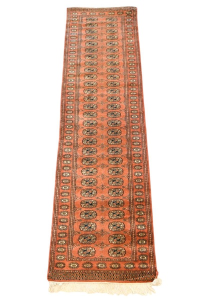 Tapete oriental tipo passadeira, medindo 293 x 77 cm, com decoração geométrica repetitiva em tons de terracota, bege e azul; apresenta desgastes compatíveis com o uso e a idade, pequenas perdas nas ex