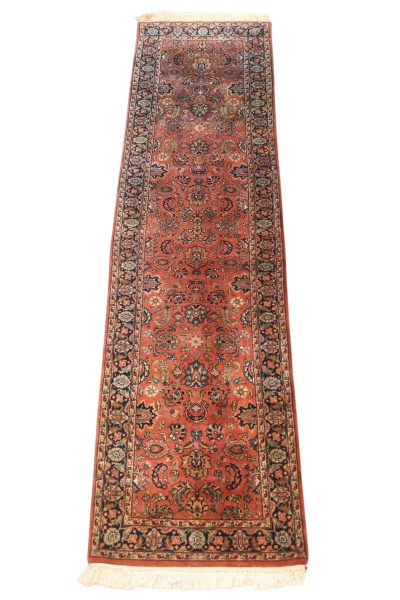 Tapete passadeira estilo oriental com decoração floral policromada sobre fundo avermelhado, medindo 310 x 80 cm; apresenta sinais de uso, leves desgastes, pequenas marcas do tempo e franjas com desgas