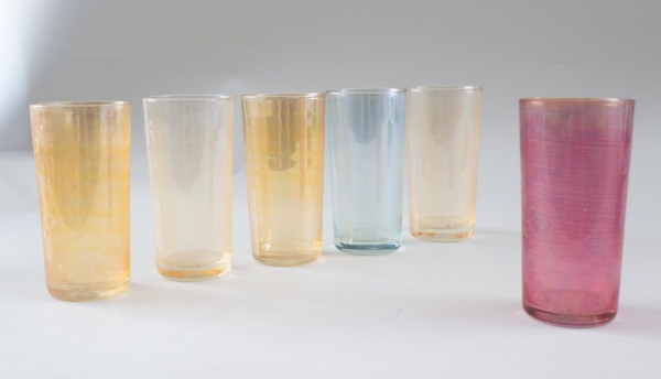 Lote contendo 6 copos em vidro iridescente colorido, sendo quatro em tom âmbar, um azul e um rosa, com acabamento perolizado. Medindo 15 cm de altura. Peças com marcas do tempo, desgastes e sinais de
