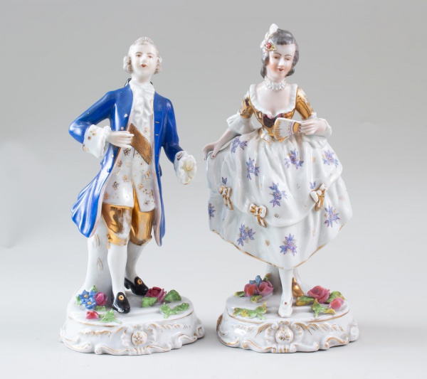 Par de esculturas em porcelana representando casal em trajes de época, ricamente decoradas com policromia e detalhes dourados, marca Vigras de Castro Rio na base, medindo 25 cm de altura; apresenta si