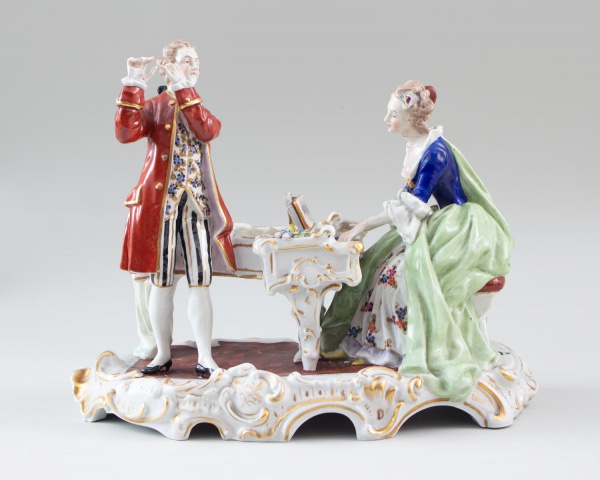 Escultura em porcelana representando cena galante de época com casal junto a piano, com decoração policromada e detalhes dourados, sobre base ornamentada, medindo 25 cm de altura e 30 cm de largura; a