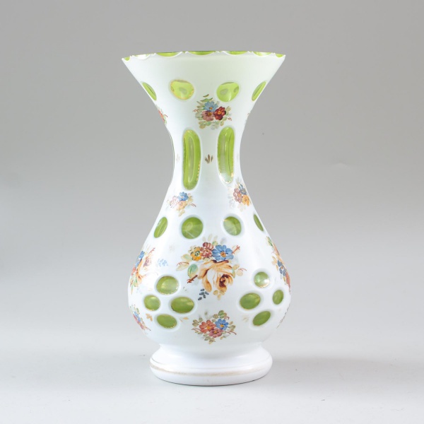 Vaso em cristal overlay, nas cores branca e verde, decorado com reservas ovais e motivos florais policromados, medindo 25 cm de altura; apresenta sinais de uso, marcas do tempo e desgastes.