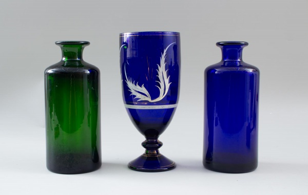 Lote contendo dois frascos decorativos em vidro nas cores verde e azul e uma taça em vidro azul com decoração gravada, maior medindo 25 cm de altura; apresentam sinais de uso, marcas do tempo e pequen