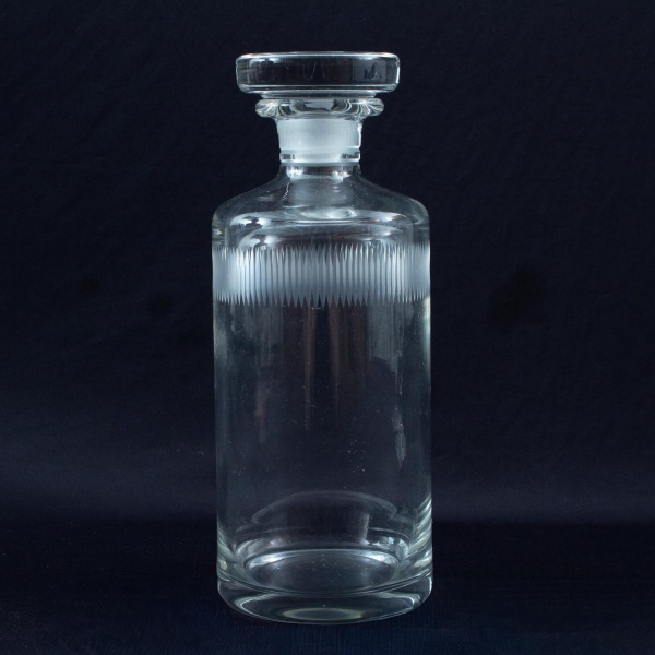 Garrafa licoreira em cristal incolor, com tampa original e decoração canelada em faixa na parte superior do corpo, medindo 25 cm de altura; apresenta sinais de uso, marcas do tempo e pequenos desgaste