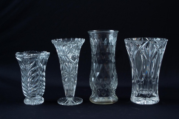 Lote contendo quatro vasos em cristal incolor, de formatos e lapidações variadas, medindo o maior 22 cm de altura; apresentam sinais de uso, marcas do tempo e pequenos desgastes.