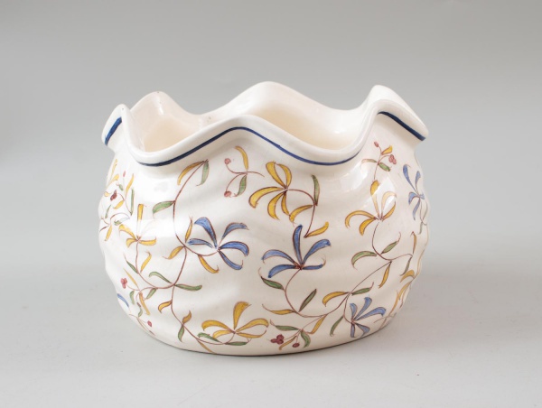 Cachepot em porcelana decorada com motivos florais policromados e borda ondulada, peça de formato sextavado. Medindo 13 cm de altura. Apresenta feltros colados na base, marcas do tempo, desgastes e si