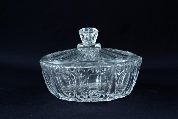 Bomboniere em cristal incolor com tampa, corpo facetado e decoração geométrica em relevo, medindo 15 cm de altura por 22 cm de diâmetro; apresenta sinais de uso e marcas do tempo.