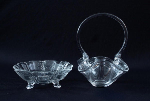 Lote contendo 2 peças em vidro incolor, sendo uma cesta decorativa com alça e uma floreira de apoio sobre pés; altura da cesta 22 cm; apresenta marcas do tempo e sinais de uso.