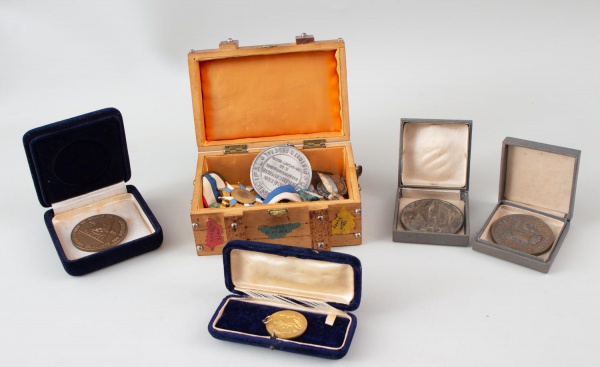Lote contendo medalhas, condecorações, distintivos, placas comemorativas, estojos e caixa decorativa em madeira; peças de diferentes épocas e instituições; apresenta marcas do tempo, oxidação, desgast