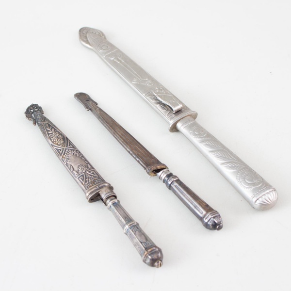 Lote contendo três facas gaúchas antigas com bainhas decoradas em metal, apresentando relevos ornamentais; com marcas do tempo, oxidação, desgastes e sinais de uso.
