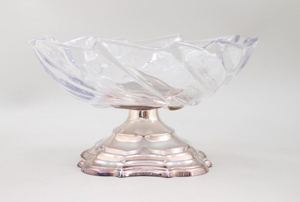 Centro de mesa em vidro incolor com base metálica, medindo 17 cm de altura e 29 cm de diâmetro; apresenta sinais de uso e marcas do tempo.