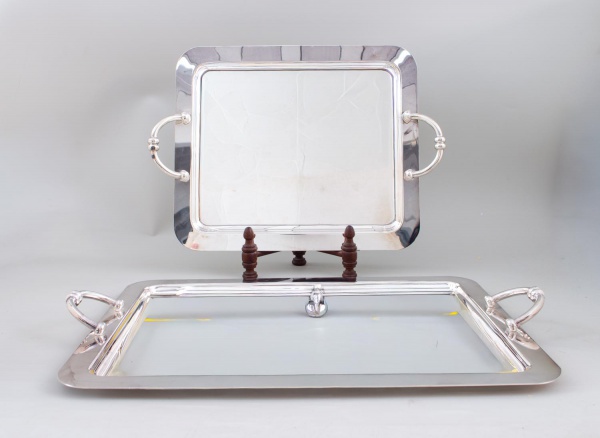 Par de bandejas retangulares em metal prateado com alças laterais vazadas, medindo a maior 47 cm de comprimento; apresentam sinais de uso, marcas do tempo, riscos superficiais e pequenos desgastes.