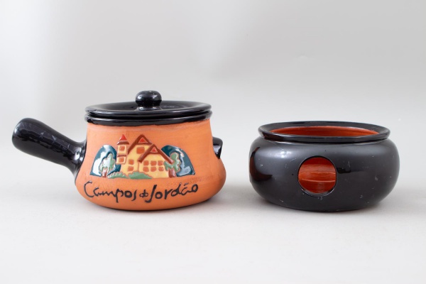 Fondue em terracota esmaltada decorada Campos do Jordão, com tampa, cabo lateral e suporte para vela; mede 11 cm de altura e 17 cm de diâmetro; apresenta sinais de uso, marcas do tempo e pequenos desg