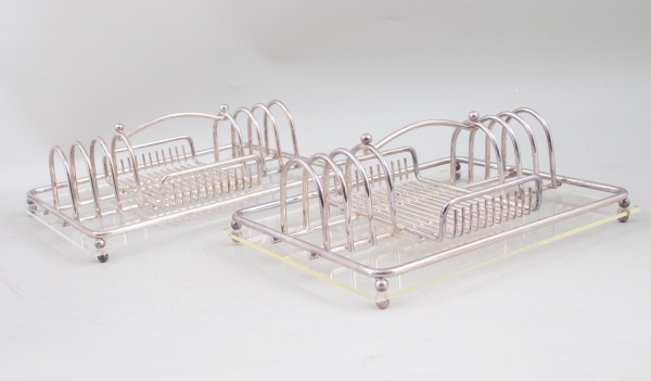 Par de suporte de talheres/escorredor em metal prateado, com base em acrílico transparente; apresentam sinais de uso, riscos superficiais e marcas do tempo.