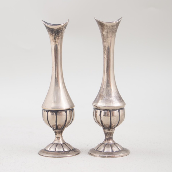 Par de castiçais em metal prateado, marca John Somers, medindo 23 cm de altura; apresentam sinais de uso, marcas do tempo e pequenos desgastes.