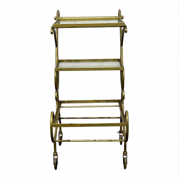 Carrinho de chá/bar em metal dourado com duas prateleiras de vidro e rodízios, medindo 80 cm de altura e 70 x 42 cm; apresenta desgastes na pintura, marcas do tempo, falta de um dos vidros e vidros re