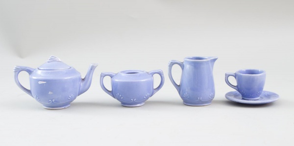 Mini conjunto para chá em cerâmica esmaltada azul, composto por bule com tampa, leiteira, açucareiro, xícara e pires, medindo a maior peça 6 cm de altura; apresentam marcas de uso e sinais do tempo.