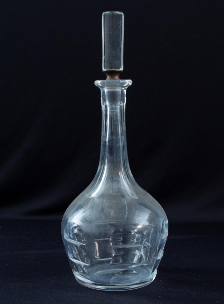Garrafa licoreira em cristal lapidado com tampa original, corpo bojudo e gargalo alongado, medindo 30 cm de altura; apresenta marcas de uso e sinais do tempo.