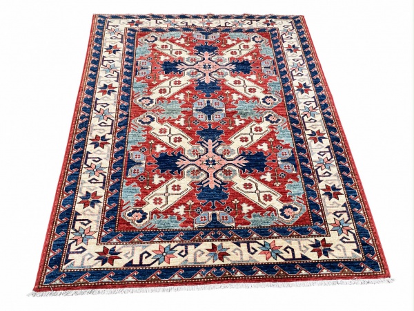Tapete com decoração geométrica em tons de vermelho, azul, bege e rosa, medindo 202 x 148 cm; apresenta franjas nas extremidades e é vendido no estado em que se encontra.