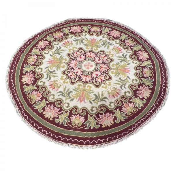 Tapete redondo com decoração floral em tons de vinho, creme, rosa e verde; medindo 187 cm de diâmetro; apresenta rasgo conforme fotos, sinais de uso e marcas do tempo; vendido no estado.