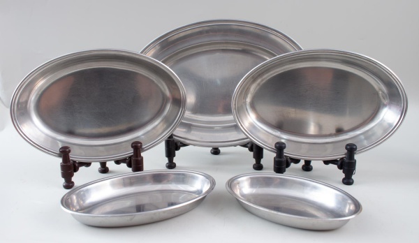Lote contendo 5 travessas ovais em metal inox, de tamanhos diversos, medindo a maior 37 x 25 cm, apresentando sinais de uso, riscos superficiais e marcas do tempo.