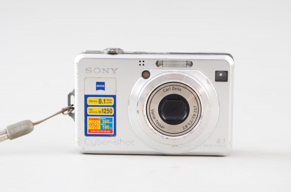 Câmera digital Sony Cyber-shot DSC-W100, 8.1 megapixels, lente Carl Zeiss Vario-Tessar, acompanha estojo; apresenta sinais de uso, riscos, marcas do tempo e oxidação superficial na parte frontal. Esta