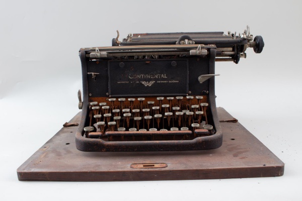 Máquina de escrever Continental Wanderer-Werke, com teclado padrão QWERTY, montada sobre base de madeira, medindo aproximadamente 22 cm de altura e 45 x 45 cm; apresenta oxidação acentuada, ferrugem e