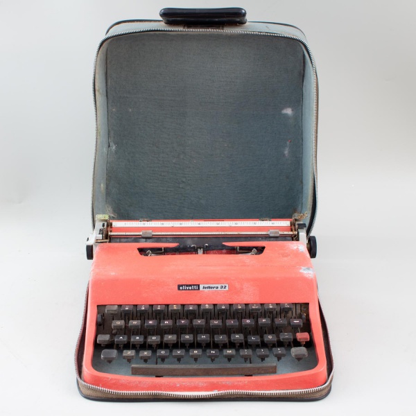 Máquina de escrever portátil Olivetti Lettera 32, na cor vermelha, acompanhada de estojo original, medindo aproximadamente 12 cm de altura e 35 cm de comprimento; apresenta marcas de uso, riscos, desg