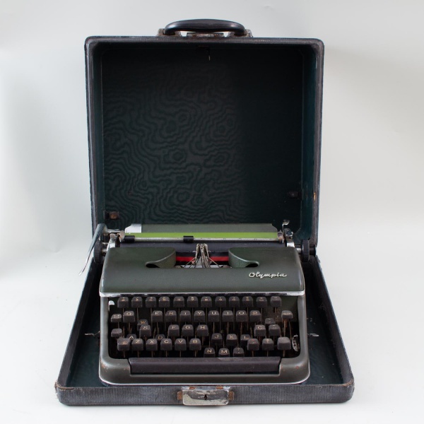 Máquina de escrever portátil Olympia, acompanhada de estojo original, medindo aproximadamente 17 cm de altura e 35 x 36 cm; apresenta marcas de uso, riscos, desgastes, oxidação pontual, sujeira e sina