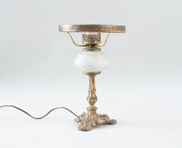 Abajur de mesa em metal dourado com rica decoração em relevo, base trabalhada e detalhe central em vidro fosco lapidado, medindo aproximadamente 29 cm de altura e 18 cm de diâmetro. Apresenta marcas d