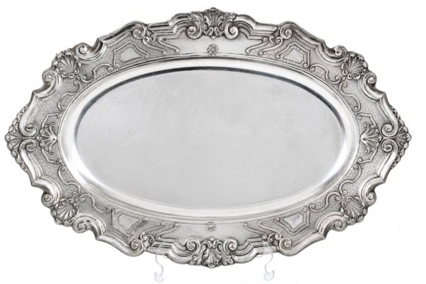 Bandeja de prata teor 833, formato oval com bordas ricamente ornamentadas em relevo com motivos concheados e arabescos, pesando 1.897 g; apresenta sinais de uso, riscos superficiais e marcas do tempo.