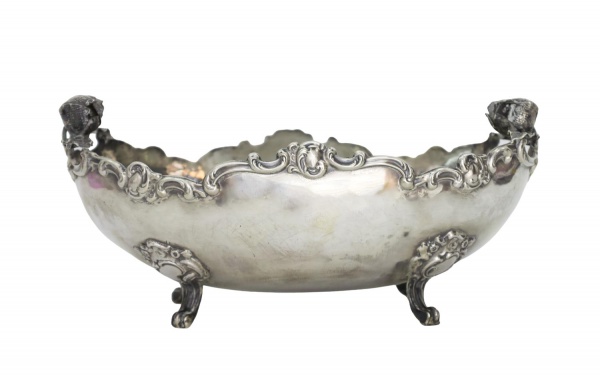 Centro de mesa em prata teor 925, formato oval, apoiado sobre pés, com bordas recortadas e decoração em relevo com motivos de cachos de uvas e volutas, medindo 32 cm de comprimento e pesando 785 g; ap