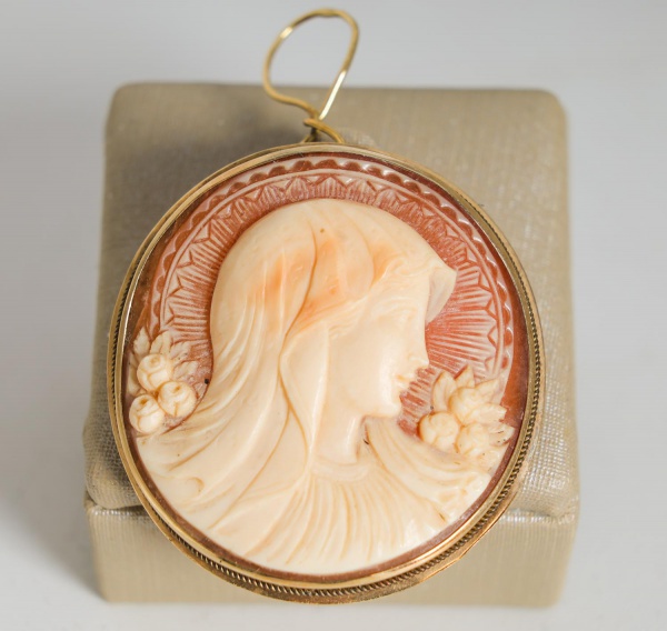 Broche em ouro 16K com camafeu oval esculpido em relevo, representando perfil feminino adornado por flores, montado em moldura lisa de ouro amarelo, pesando 6,7 g