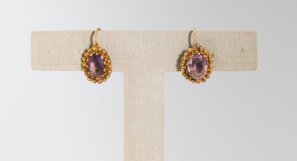 Par de brincos em ouro amarelo 18K, com pedras roxas em lapidação oval facetada, engastadas em molduras ornamentadas com acabamento em granulação, pesando ao todo 3,4 g;