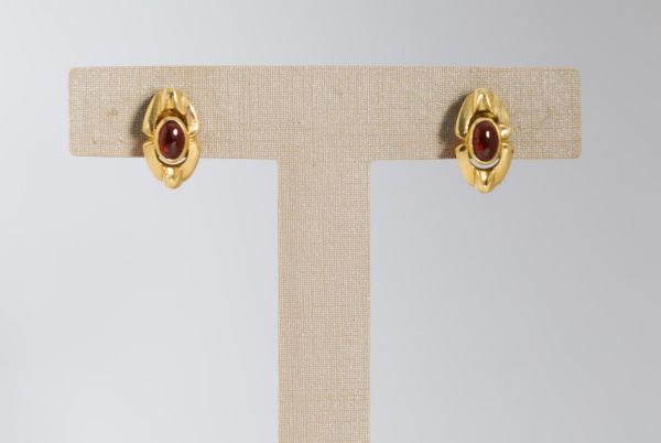 Par de brincos em ouro amarelo 18K, com design entrelaçado e aplicação central de pedras vermelhas em formato oval cabochão, pesando ao todo 3,7 g