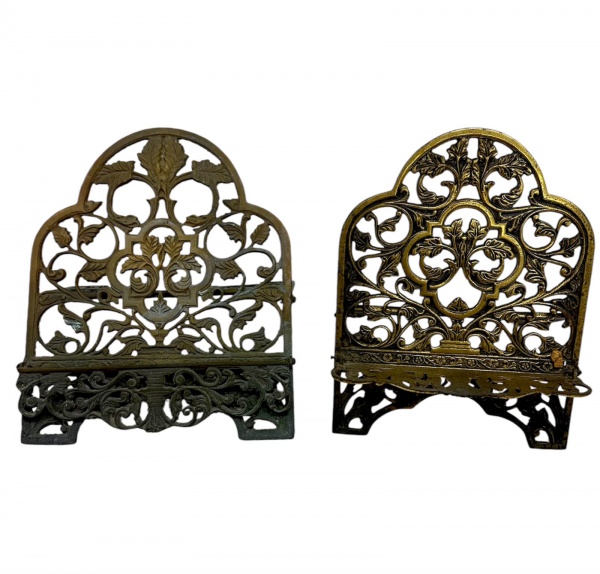 Par de porta-livros em metal dourado com decoração vazada em motivos florais e arabescos; o maior medindo 35 cm de altura, 22 cm de profundidade e 29 cm de largura; apresenta marcas do tempo, desgaste