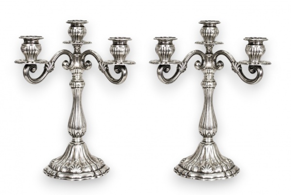 Par de candelabros em prata de lei peruana, teor 925 milésimas, de cinco luzes cada, executados em estilo Rococó, de linhas elegantes e ornamentação contida. Cada peça assenta sobre base circular de p