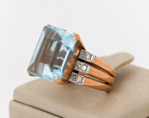 Anel em ouro amarelo 18k (750), aro 14, com expressiva pedra central em lapidação retangular facetada, de tonalidade azul-claro (possivelmente água-marinha ou topázio azul), em robusta caixa alta com