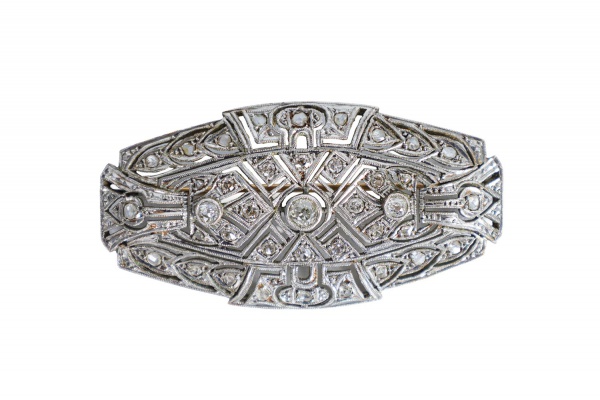 Broche em ouro branco 16k, estilo Art Déco, ricamente trabalhado em delicada composição geométrica vazada e adornado com múltiplos brilhantes em cravação. Apresenta elegante desenho simétrico com acab