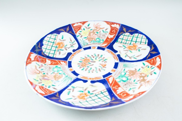 Prato decorativo em porcelana oriental com aba larga, decorado em policromia com reservas contendo motivos florais, aves e elementos geométricos em azul, vermelho e verde, medindo 40 cm de diâmetro, a