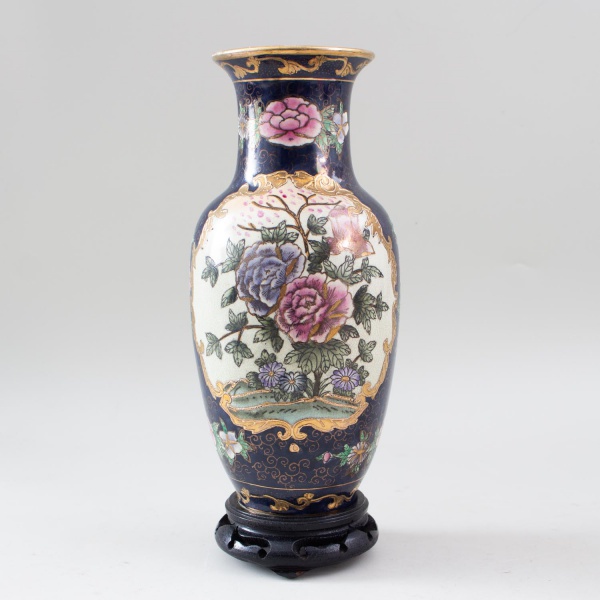 Vaso em cerâmica esmaltada com decoração oriental em policromia representando flores e folhagens, enriquecida por detalhes em dourado sobre fundo azul cobalto, apoiado sobre base de madeira entalhada,